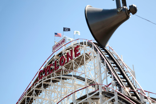 Coney Island, NY - June 22, 2007: Landmark Cyclone wooden rollercoaster in the famous Astroland amusement park with loud speaker in the foreground and AMerican and POW flangs on the top of the coaster