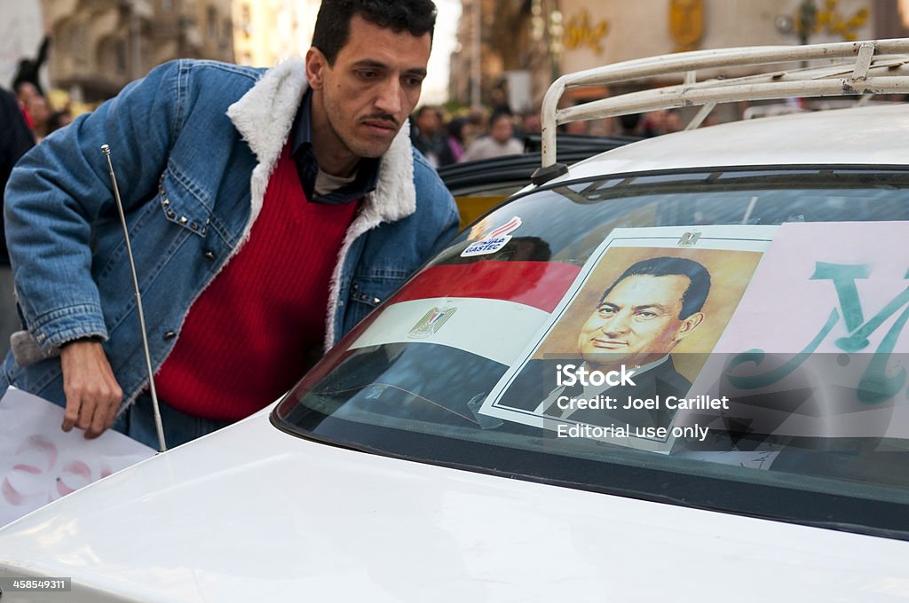 Egypt's Hosni Mubarak Cairo, Egypt - February 2, 2011: During the political upheaval that would soon lead to the resignation of Egyptian President Hosni Mubarak, a supporter of the president stands outside a car in Talaat Harb Square. The car is displaying an Egyptian flag and presidential portrait. Cairo Stock Photo