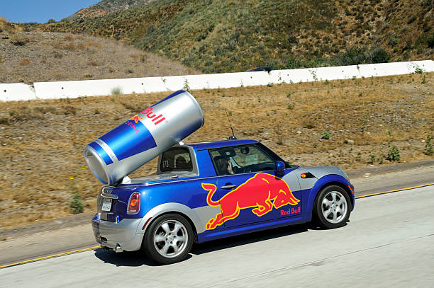 red bull mini cooper Devore, California, USA - September 19, 2010: A custom painted BMW Mini Cooper Cabriolet with a large can of Red Bull energy drink mounted to the top traveling south down interstate 15 with a driver and passenger. red bull mini stock pictures, royalty-free photos & images