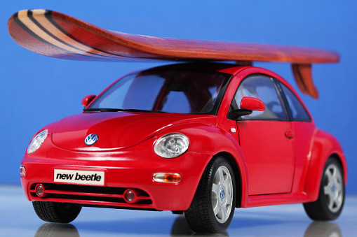 Cantley, Quebec, Canada - February 20, 2009: Red Toy car Volkswagen New Beetle with wood surfboard on car roof with a blue background. This Red Volkswagen New Beetle is the Special Edition 1:25 product by Maisto. Maisto was founded in 1967 and is a company that manufactures die-cast models of aircraft, motorcycles and automobiles. The small wooden surfboard decoration have no brand-name on it.
