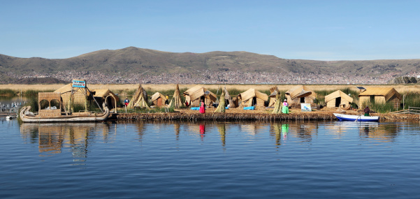 Los Uros Islands, Peru - December 12,2009: Typical village with reed huts and reed boats made in floating islands on Lake Titicaca. Peruvian people making their daily works. The city of Puno is in the background. Lake Titicaca is the largest lake in South America and it\'s partially in Peru and partially in Bolivia.One of the main attractions on the lake are the Uros floating islands made of floating reeds (totora reed).