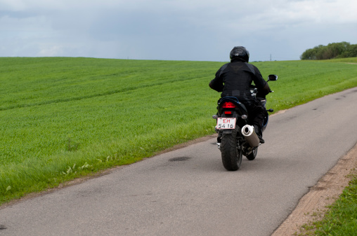 Taastrup, Denmark - June 6th, 2010: Man rides a blue Suzuki motorcycle on a small country road. He is all alone on the road and passes by green fields.