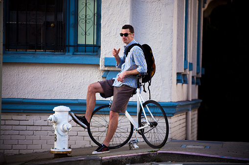 San Francisco, California - January 30, 2010: A roung man wearing headphones and sunglasses and riding a fixed-gear bicycle leans on his bike at the top of a hill in San Francisco, California