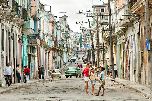 Havana, Cuba - January 1, 2011: Three Cuban children playing one of narrow streets in the center of La Havana. Colonial architecture, old cars driving or parked at the street, Cuban people walking all around.