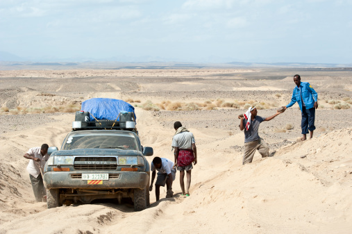 Erta Ale district, Ethiopia - November 27, 2011: A heavy loaded 4WD car of the tourist group has got stucked on a sandy road, five Ethiopians are trying to get car going again. The person on the right with the blue shirt is a local Afar policeman who should protect the tourists and their Ethopian helpers in the Afar region. The Danakil Desert in the Danakil Depression/Afar triangle in the borderland between Ethiopia, Eritrea and Djibouti is one of the most remote and most extreme regions of the world - it is the lowest point in Africa (- 155 metres/- 550 ft below sea level).