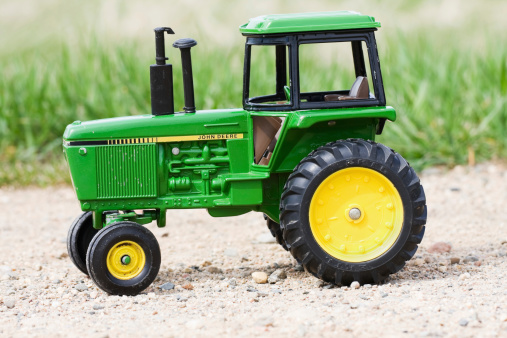 Fosston, USA - May 18, 2011:  A John Deere replica collectible toy tractor made by The Ertl Company.  The tractor is outdoors on a gravel road with grass in the background.  Please note that the tractor is not new and has some scratches and chips.