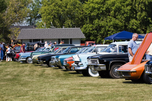 Fosston, USA - August 27, 2011:  People viewing collector\'s cars that are parked in a row at a classic car show.  In the front, a man is looking under the open hood of an orange Chevrolet Corvette.