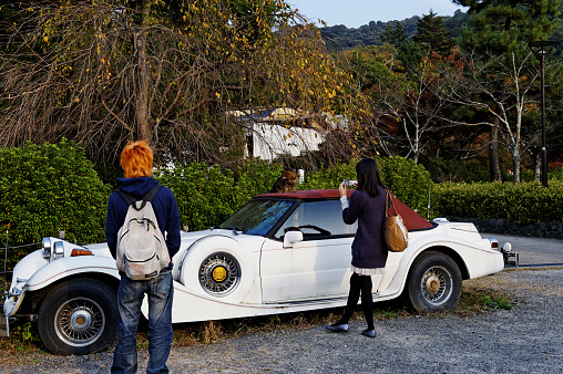 Kyoto, Japan - November 14, 2010: Young Japanese woman taking on picture of a cat sitting on the roof of a stationary CMC (Classic Motor Carriages) Tiffany Classic vintage car. A young man with orange hair  is watching.