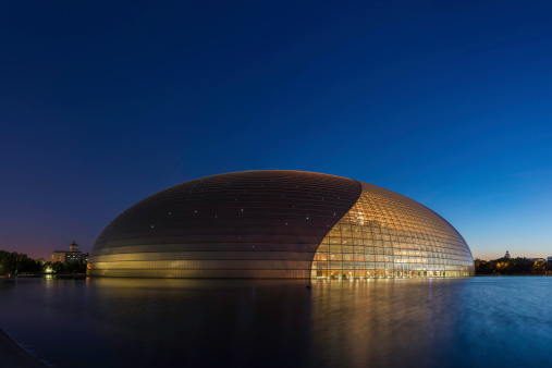Beijing, China - 24th September 2013: Stars shining in the chrome blue dusk skies above the graceful curves and warm glow of the National Centre for the Performing Arts, Beijing's futuristic opera house, theatre and arts complex, reflecting in the tranquil waters of the surrounding lake beside Tiananmen Square in the heart of China's vibrant capital city. Composite panoramic image created from five contemporaneous sequential photographs.