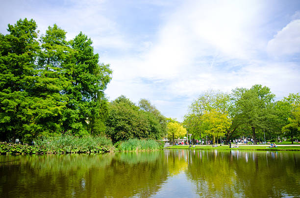 Amsterdam, Netherlands - August 17, 2011: People relax along grass next to a pond at the public park known as Vondelpark in Amsterdam.