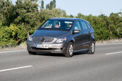 Wiesbaden, Germany - June 2, 2011: A couple in a grey-metallic 5-door Mercedes-Benz B-Class (T245) drives on a road through the Rheingau near Wiesbaden, Germany. The B-Class-cars (also known as T245-series) are compact MPV cars, the first generation started in 2005. Mercedes-Benz is a German manufacturer of automobiles and trucks and a division of Daimler AG, formerly Daimler-Chrysler. Some minor motion blur