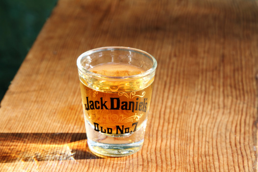 West Palm Beach, USA - September 17, 2011: This image shows a shot glass with the Jack Daniels brand name and design filled with Jack Daniel's Old No 7 Whiskey. The shot glass is setting on an outdoor wood table with the late afternoon sun shining through and illuminating the whiskey.