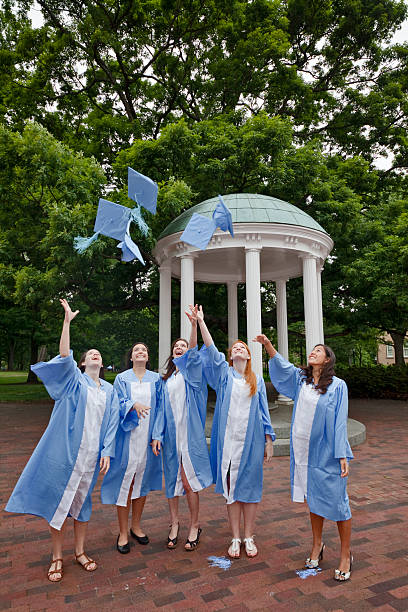 Five UNC senior college students practicing the traditional cap throw Chapel Hill, North Carolina, USA - April 28, 2012: Five female senior undergraduate students who are about to graduate with a bachelors degree are wearing their light blue colored cap and gown and are practicing the cap toss in front of the Old Well chapel hill photos stock pictures, royalty-free photos & images