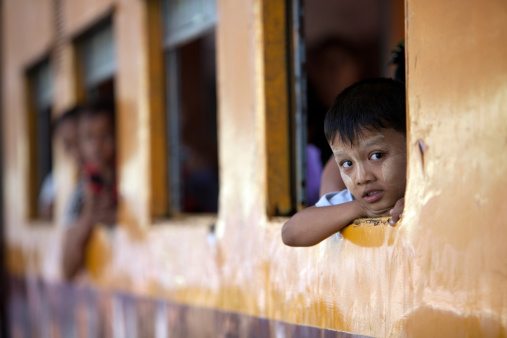 Yangon, Myanmar - February 25, 2011:A young boy rests his arms and head on the train window to look outside at leisure whilst waiting for the train to leave Yangon station. The Yangon central railway station is the largest station in Myanmar, the design based on Burmese style architecture. The trains mostly connect only the major cities and are largely government run. There are only two private companies running trains, the quality of which is better than the government run trains.