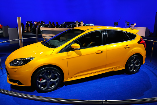 Brussels, Belgium - January 10, 2012: Orange Ford Focus ST hatchback on display during the 2012 Brussels motor show. People in the background are looking at the cars.