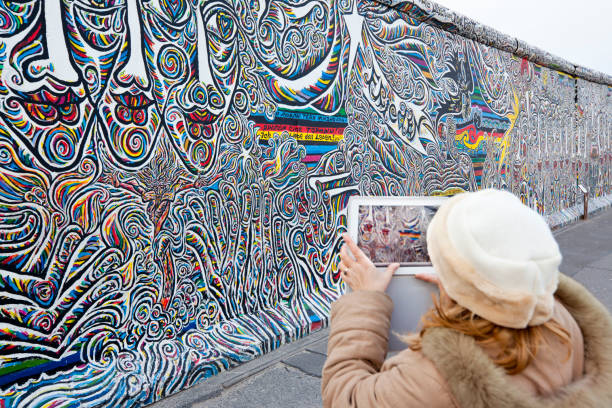 Berlin, Germany - January 4, 2012: Tourist taking a photo at the outdoor Gallery called East Side Gallery in Berlin. From 1990 several artists did huge paintings on the remnants of the Berlin Wall along Muehlenstrasse at the Spree river (1316 meters overall). This painting is from Schamil Gimajev and has no title.