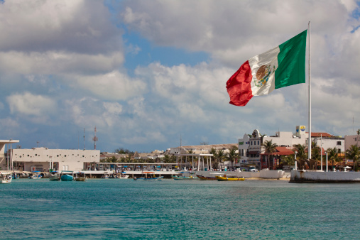 Playa Del Carmen, Mexico - February, 2nd  2011:  Ferry port to Cozumel showing everyday life and a  massive Mexican flag flying high in front of the shopping district.