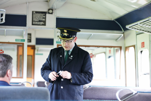 Carmarthen, Wales - August 19, 2011: Railway Guard in authentic period railway uniform on the train at the Gwili Steam Railway a preserved UK railway in the Welsh countryside on the outskirts of Carmarthen. He is punching a passenger's ticket on a diesel multiple unit from the 1960s.