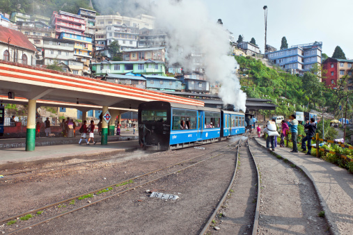 Darjeeling, West Bengal, India - May 18th, 2012: Steam engine of old Toy Train (N.F.795B)in the city of Darjeeling; people walking, photographing, working in the background, St. Columba's Church on the left.