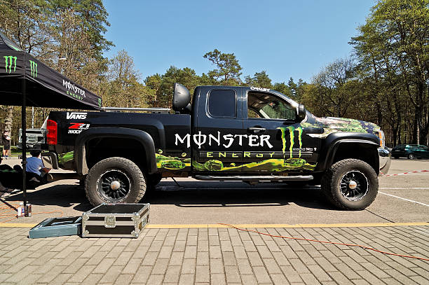 Monster Energy truck Druskininkai, Lithuania - April 28, 2012: Monster Energy truck Chevrolet Silverado Z71 all covered with Monster Energy stickers parked at parking lot near Monster Energy tent at first in Lithuania Longboard Day event at resort Druskininkai in Lithuania. People sitting on the couches under the tent at chill zone and watching the event. chevrolet silverado stock pictures, royalty-free photos & images