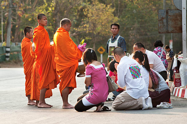 Chiang Mai, Thailand - March 1, 2011: Buddhist monks wearing traditional orange robes walk the streets in the early morning to receive offerings of food from the public in Chiang Mai, Thailand.