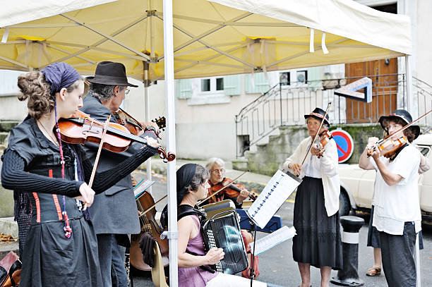 Dieulefit, France - August 7, 2011: French musicians in the gypsy style, wearing traditional headscarves or Provencal hats and playing violins, viola, cello and accordion. Their ages range from 30s to 80+ (the lady at the back playing the violin) and all are concentrating on their music. The band is composed of local people and is playing outdoors on the street as part of a village festival in Provence, France. Throughout the summer both local and visiting entertainment acts offer entertainment of this style in the south of France.