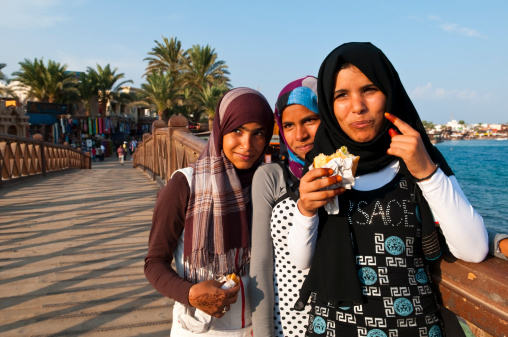 Dahab, Egypt - November 16, 2010: Three Bedouin girls stand on a pedestrian bridge in this Sinai town situated on the Gulf of Aqaba. Two are eating and have henna on their hands.