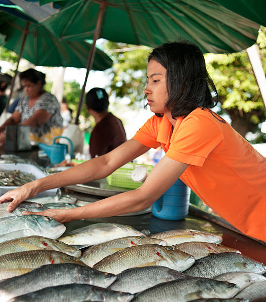 Rawai, Phuket, Thailand - April 26, 2011: A young woman wearing a bright orange shirt selling fish at a street market in Rawai, Phuket, Thailand. This is a sea gypsy market on the edge of a slum area in the south of Phuket.