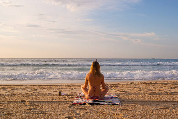 Bondi Babe Sydney, Australia - April 7, 2012: A girl in swimwear sitting on a beach towel on Bondi Beach looks towards the sea just after sunrise. bondi beach sunrise stock pictures, royalty-free photos & images