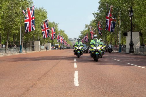 London, UK- April 28, 2011: Police escort drives up The Mall towards Buckingham Palace. Union Jack flags line The Mall in preparation for the Royal Wedding, the next day, on the April 29, 2011. Tourists crowd the pavements on both sides of the street as they walk to see Buckingham Palace. Admiralty Arch can be seen in the distance, behind the Police escort.