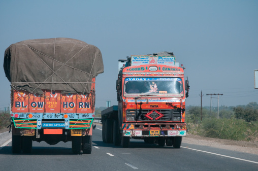 Road to Jaipur, India - January 8, 2011: Two trucks on the main highway road connecting Udaipur and Jaipur in Rajasthan. Indian trucks are generally hopelessly overloaded and in bad condition. Every truck is painted individually by specialised companies. This truck is carrying goods, boxes held together by cord.