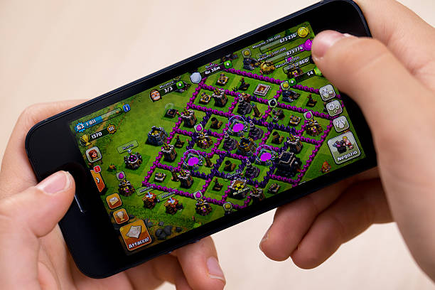 Milan, Italy - October 17, 2013: Woman hand holding Apple iPhone 5. Apple iPhone 5 displaying iOS 7 with 'Clash of Clans' application. iOS 7 is the latest mobile operating system designed by Apple Inc. Clash of Clans is one of the most popular games of Apple world