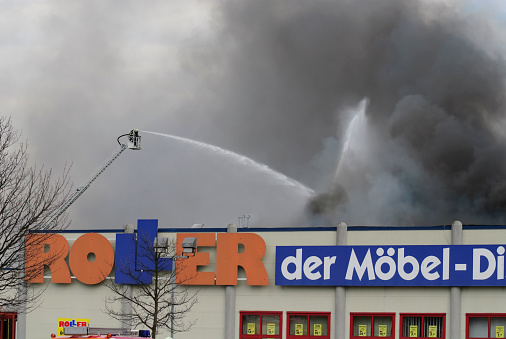 Eisenhuettenstadt, Germany - March 21, 2010: Great Fire in a shopping mall and furniture store, Eisenhuettenstadt, Brandenburg, Germany. Firefighters in action on the roof of the warehouse. Dense smoke over the camp of the furniture store.