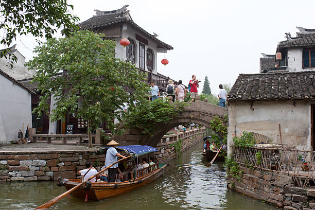 Water Town Zhouzhuang, China Zhouzhuang, China - July, 15th 2007 : Many tourists go sightseeing in Zhouzhuang Town of Kunshan City, Jiangsu Province, China. Some tourists are walking on a historic bridge, some tourists are sitting on the boats to enjoy the sightseeing in water town. Zhouzhuang, first built around 1,000 years ago, is one of the most famous water townships in China, noted for its profound cultural background, the well preserved ancient residential houses, the elegant watery views and the colourful local traditions and folklore. Sixty percent of Zhouzhuang\'s structures were built during the Ming and Qing Dynasties from 1368 to 1911. water town zhouzhuang china stock pictures, royalty-free photos & images