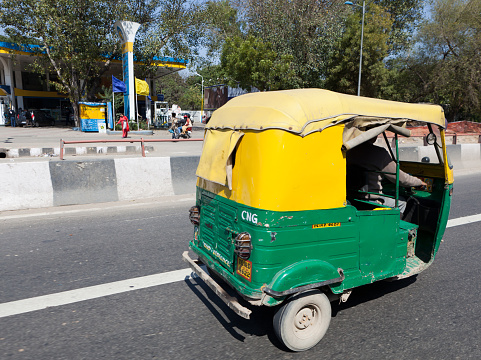 Delhi, India - March 6, 2011: Green-yellow car rickshaw  in downtown from capital Dehli in India. In common speech they are called 'Tuc-Tuc'. In the background people are pass by.