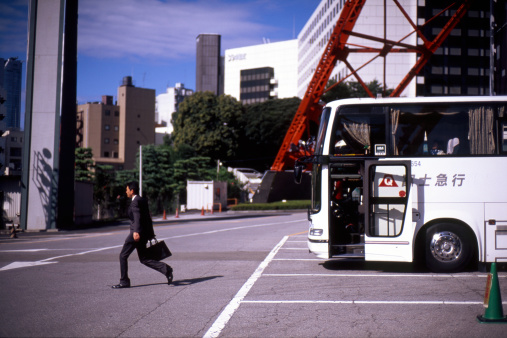 Tokyo, Japan - November, 2010 : A Japanese businessman walks past a bus outside the Tokyo Tower, a popular tourist attraction located in Shiba Park, Minato, Tokyo.