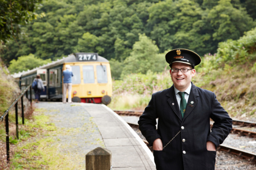 Carmarthen, Wales - August 19, 2011: Railway Guard in authentic period railway uniform on the platform at the Gwili Steam Railway a preserved UK railway in the Welsh countryside on the outskirts of Carmarthen. A diesel multiple unit from 1960 is at the platform in the background.