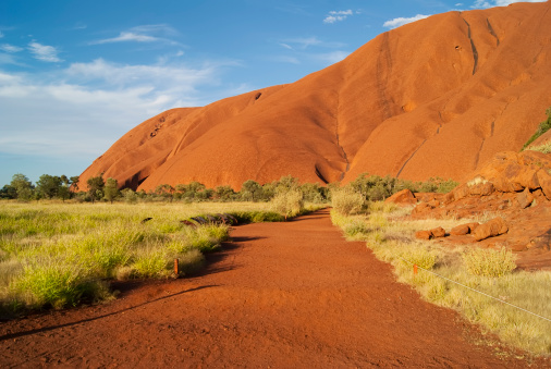 Uluru-Kata Tjuta National Park, Northern Territory, Australia - April 13, 2011: A red sand path shows the way towards Uluru. The path is part of the Mala walking trail that goes around the base of the giant monolith.