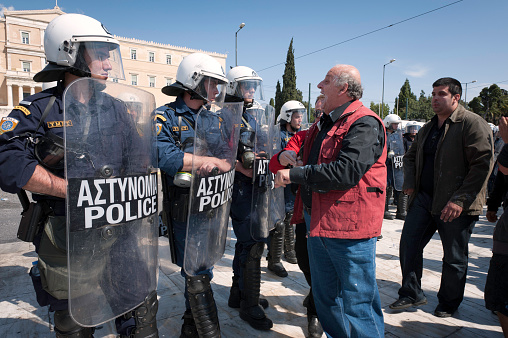 Athens, Greece - May 11, 2011: Greek riot police with shields, gas masks, clubs stand at Syntagma, Square with the Parliament building in the background. A man approaches and yells at them.