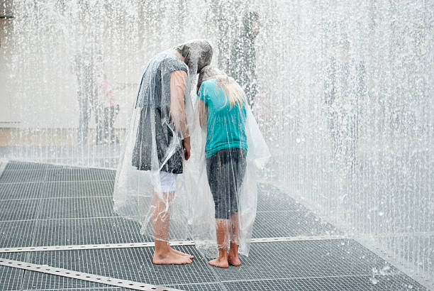 Linz, Austria - July 26,2011: Two caucasian kids with raincoat standing in a big fountain, during the art festival H&amp;amp;amp;ouml;henrausch in Linz, Upper Austria.