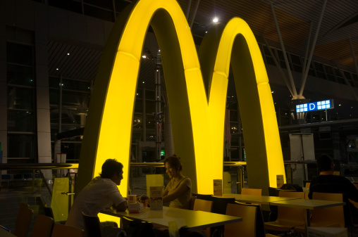 Kuching, Malaysia - October 3, 2010: Smiling asian couple eating in the McDonalds restaurant of the International airport of Kuching. It is dark, and the illuminated M-Logo of McDonalds  is shining on the tables.