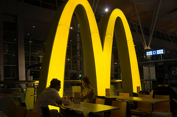 Smiling asian couple eating in McDonalds restaurant Kuching, Malaysia - October 3, 2010: Smiling asian couple eating in the McDonalds restaurant of the International airport of Kuching. It is dark, and the illuminated M-Logo of McDonalds  is shining on the tables. customs airport sign air transport building stock pictures, royalty-free photos & images