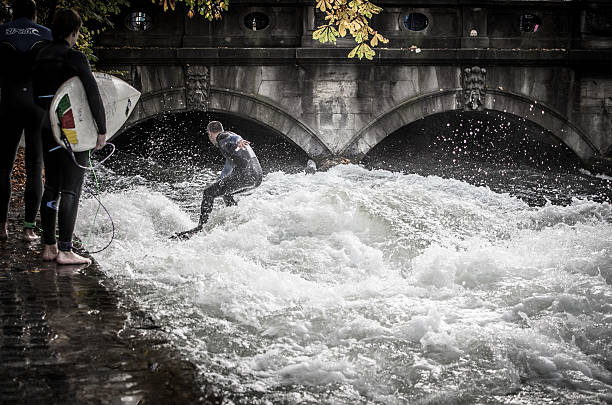 Munich Germany - October 26, 2013: Man surfing on the Eisbach river in the Englischer Garten in Munich in on autum day. Top hot spot for surfers. 2 friends are waiting