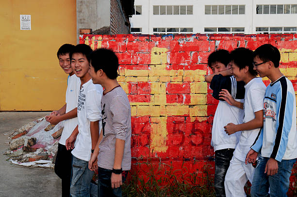 Group of Happy Chinese Teenage Boys. Taizhou, Jiangsu Province, China - October 8th, 2009: Group of six happy teenage boys walk past the Chinese symbol for Middle painted on a brick wall. fang xiang stock pictures, royalty-free photos & images