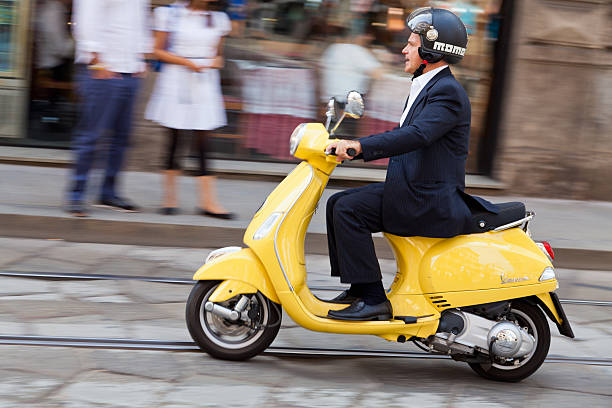 homem dirigindo seu scooter a passar nas ruas de milão - vespa scooter imagens e fotografias de stock