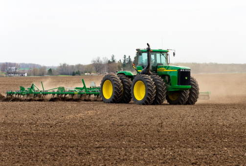 Drayton,Ontario,Canada - May 11, 2011: A farmer with a large John Deere tractor and cultvator works the land on a Spring day in Southwestern Ontario. Once the dominant industry, agriculture occupies a small percentage of the population but still a large part of Southern Ontario's land area. The number of farms has decreased from 68,633 in 1991 to 59,728 in 2001, but farms have increased in average size, and many are becoming more mechanized.
