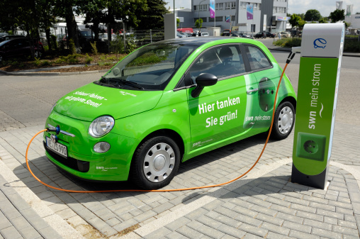 Neuss, Germany - May 13, 2011: A green FIAT 500 electric car is connected with a power chord on a recharging station. This car is used by the company swn, the energy provider and public utility company of the city Neuss. The recharging station is a cooperation with RWE, one of the biggest energy provider in Europe and it is powered with electric energy from solar panels. The label on the car door means: Green refilling.