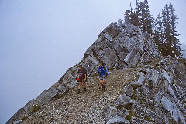 Alpine Lakes Wilderness, Washington, USA - August 01, 1995: Two women walking on the Kendall Katwalk section of the Pacific Crest Trail on a foggy day. Kendall Katwalk is a high narrow ridge in the Alpine Lakes Wilderness of Washington State. The view can be spectacular on a clear day.