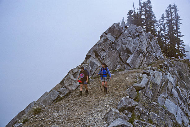 Two Hikers Walk the Pacific Crest Trail in Fog Alpine Lakes Wilderness, Washington, USA - August 01, 1995: Two women walking on the Kendall Katwalk section of the Pacific Crest Trail on a foggy day. Kendall Katwalk is a high narrow ridge in the Alpine Lakes Wilderness of Washington State. The view can be spectacular on a clear day. jeff goulden alpine lakes wilderness stock pictures, royalty-free photos & images