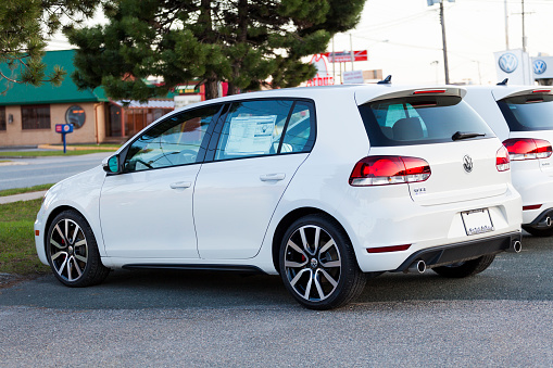 Saint John, New Brunswick, Canada - April 28, 2012: A new 2012 Volkswagen Golf GTI 2.0 TSI 6-Speed for sale and on display at a car dealership.  Identical model pictured beside and behind vehicle in focus.  In background, the Volkswagen logo and sign can be seen as well as other establishments.
